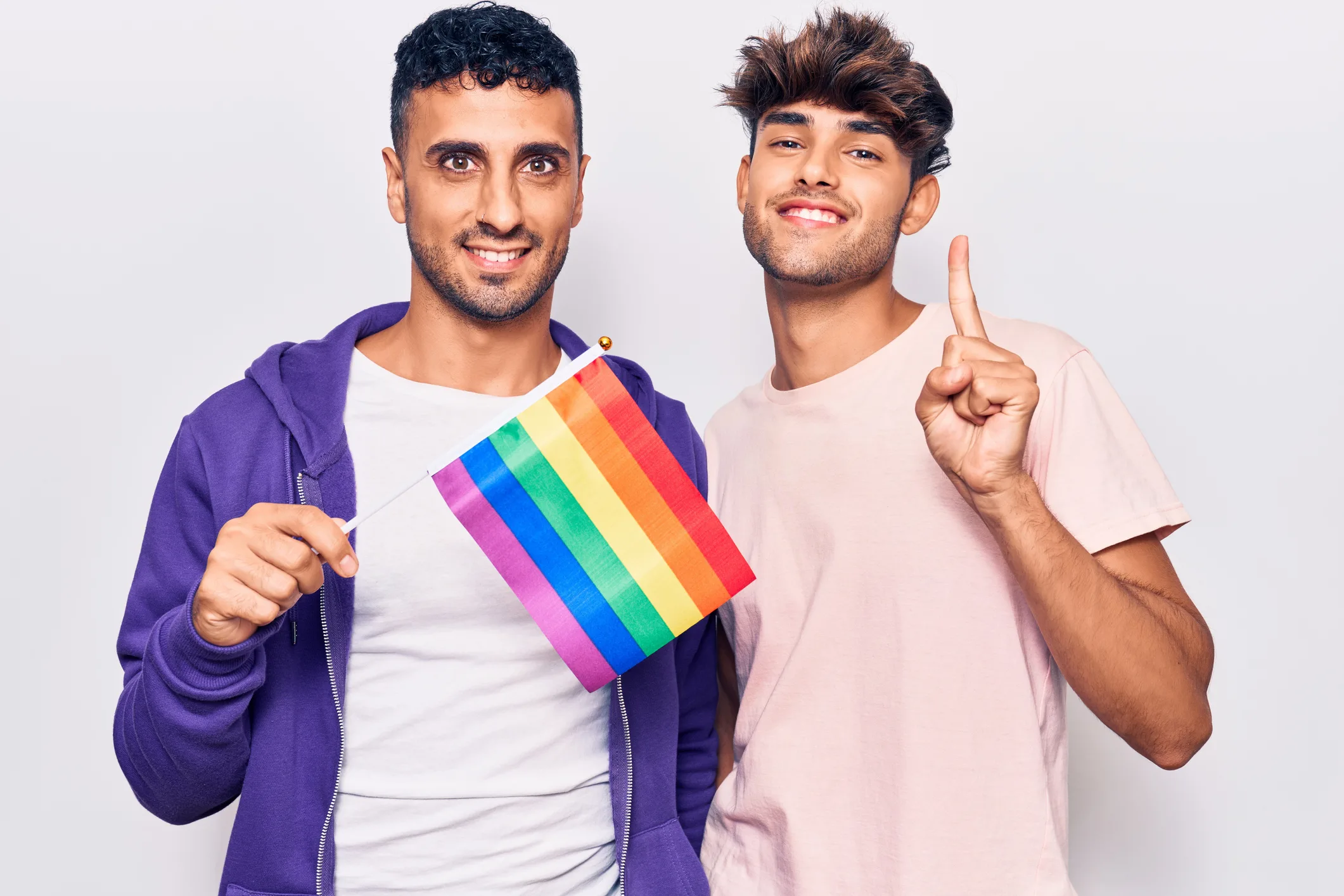 Young gay couple holding rainbow LGBTQ flag smiling
